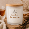 A frosted glass jar candle with a light wood lid sits on a wooden surface in a styled setting. The front label reads Arc Candles and Bourbon Butterscotch, with vanilla beans and a glass of amber liquid blurred in the background.