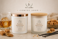 Two Arc Candle 'Bourbon Butterscotch' scented candles are displayed on a light beige surface with caramel pieces, vanilla beans, and a glass of whiskey. The left candle has a rose gold lid, and the right candle has a natural wood lid.